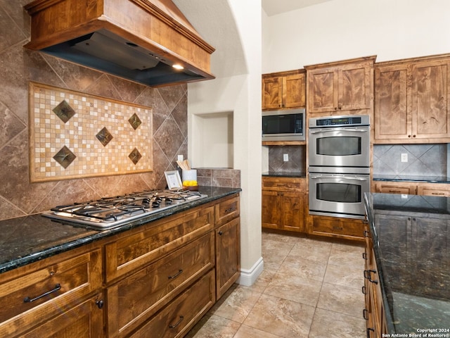 kitchen featuring stainless steel appliances, dark stone countertops, custom exhaust hood, and decorative backsplash