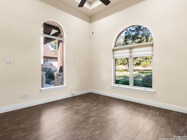 unfurnished room with a high ceiling, ceiling fan, and dark hardwood / wood-style flooring