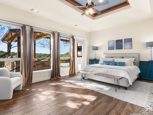 bedroom with ceiling fan, dark hardwood / wood-style floors, and a raised ceiling