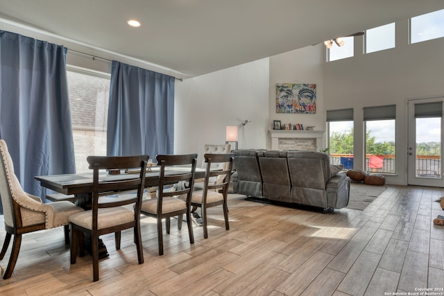 dining room with a towering ceiling, a stone fireplace, and light hardwood / wood-style flooring