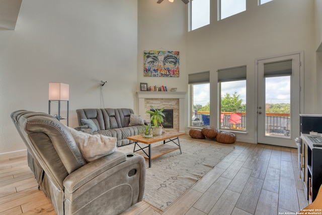 living room with ceiling fan, a towering ceiling, a stone fireplace, and light hardwood / wood-style flooring