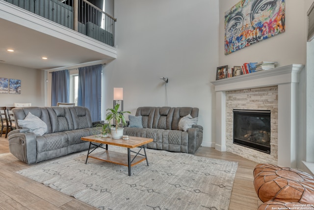 living room with a towering ceiling, a stone fireplace, and light wood-type flooring