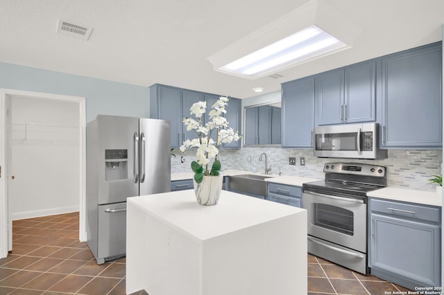 kitchen with a kitchen island, blue cabinetry, appliances with stainless steel finishes, decorative backsplash, and sink