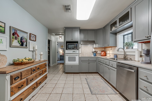 kitchen with stainless steel appliances, light tile patterned floors, gray cabinets, decorative backsplash, and sink