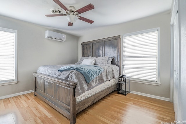 bedroom with light hardwood / wood-style floors, a wall unit AC, multiple windows, and ceiling fan