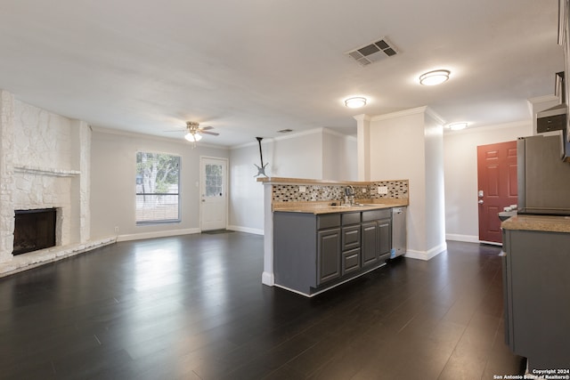 kitchen with a stone fireplace, dark wood-type flooring, sink, tasteful backsplash, and ceiling fan