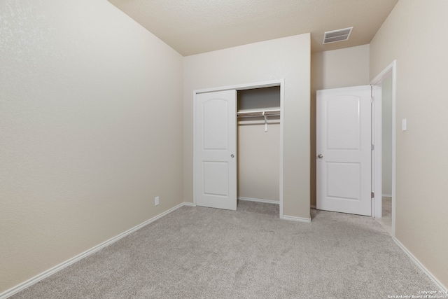 unfurnished bedroom featuring light colored carpet, a textured ceiling, and a closet