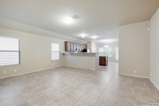 unfurnished living room with a wealth of natural light, an inviting chandelier, light tile patterned flooring, and a textured ceiling