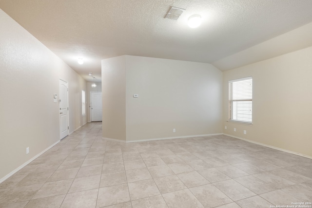 tiled empty room featuring a textured ceiling and lofted ceiling