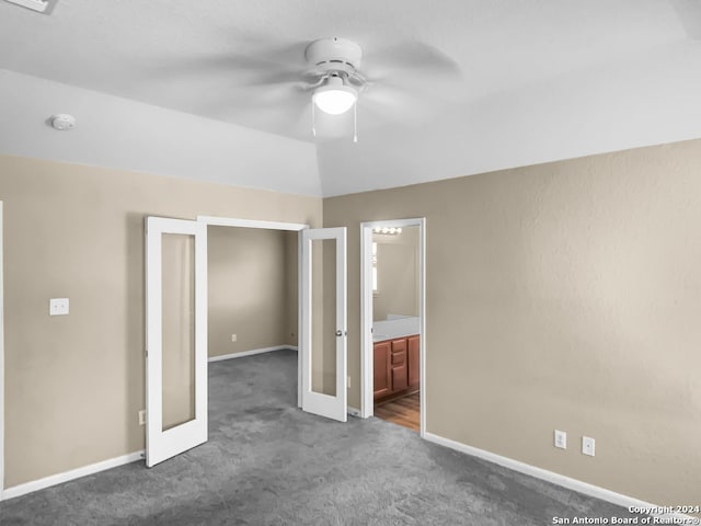 unfurnished bedroom featuring dark colored carpet, french doors, ensuite bathroom, and ceiling fan