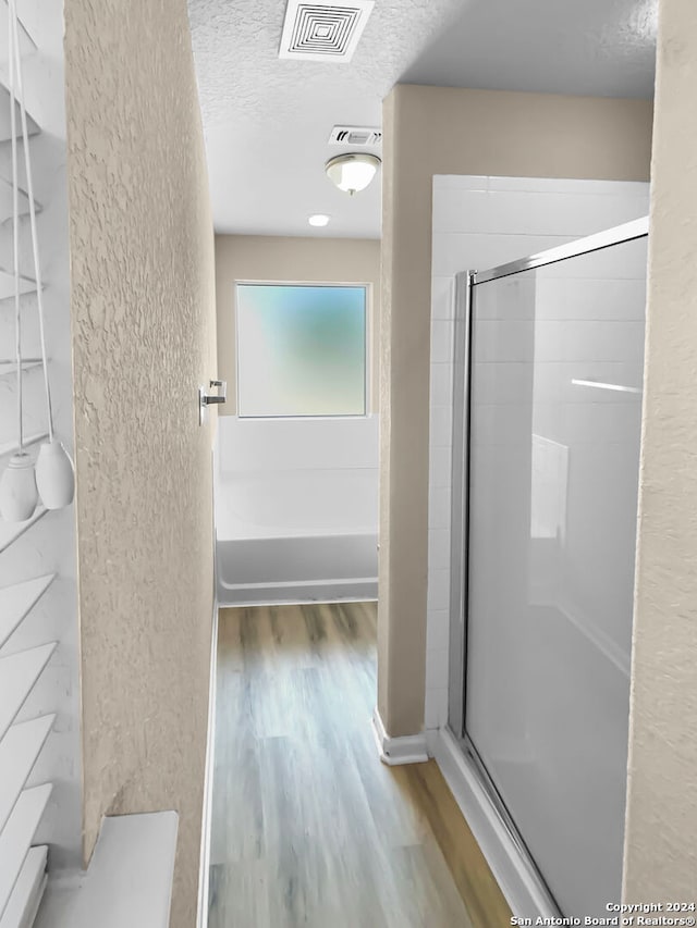 bathroom featuring a textured ceiling, wood-type flooring, and a shower with door