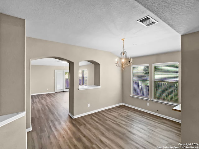 empty room with a healthy amount of sunlight, dark hardwood / wood-style flooring, a textured ceiling, and a chandelier