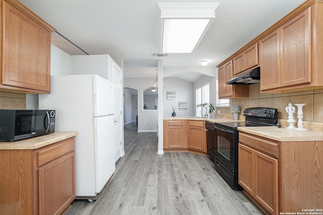 kitchen with decorative backsplash, kitchen peninsula, vaulted ceiling, black appliances, and light hardwood / wood-style flooring