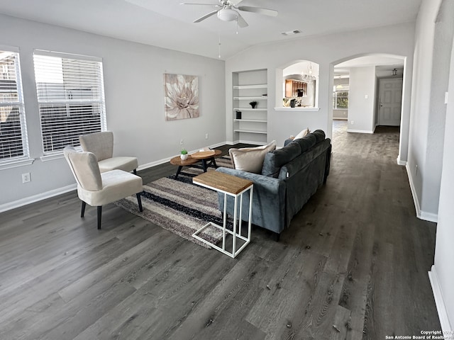 living room featuring built in shelves, ceiling fan, dark hardwood / wood-style flooring, and vaulted ceiling