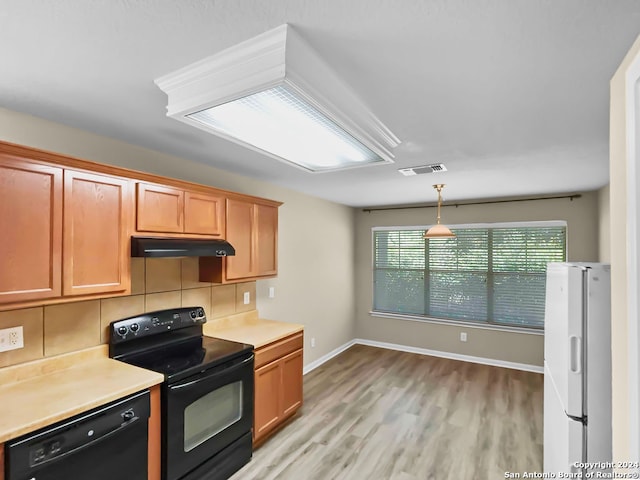 kitchen with hanging light fixtures, backsplash, light hardwood / wood-style flooring, and black appliances