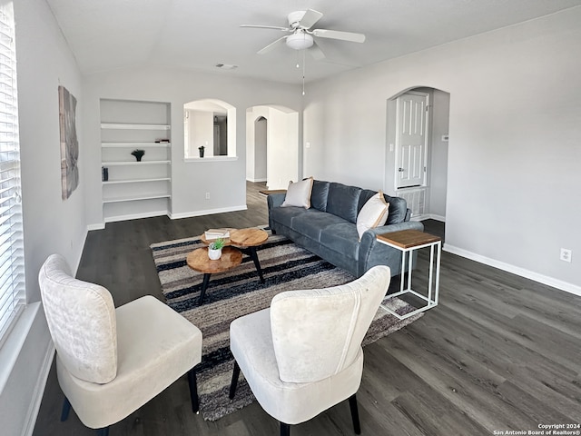 living room with built in shelves, vaulted ceiling, ceiling fan, and dark wood-type flooring