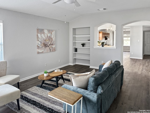 living room featuring dark wood-type flooring, built in features, a textured ceiling, vaulted ceiling, and ceiling fan with notable chandelier