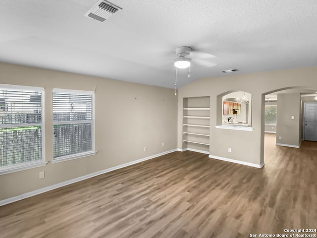 interior space with lofted ceiling, hardwood / wood-style flooring, ceiling fan, built in shelves, and a textured ceiling