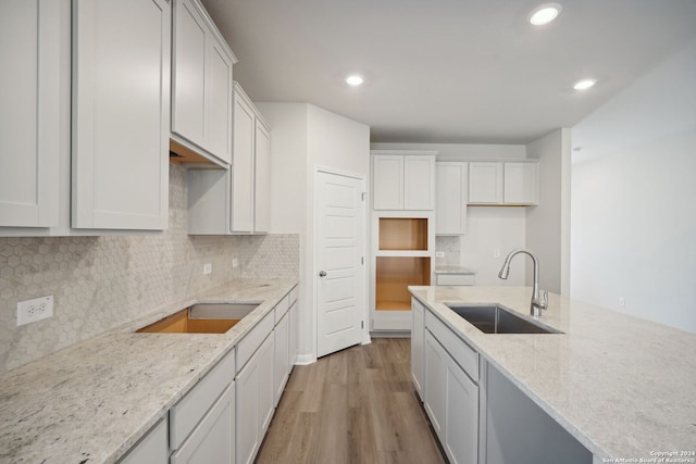 kitchen featuring light stone countertops, white cabinetry, light hardwood / wood-style flooring, and sink