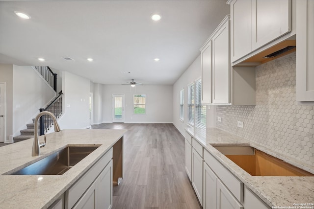 kitchen with ceiling fan, sink, light stone counters, backsplash, and light wood-type flooring