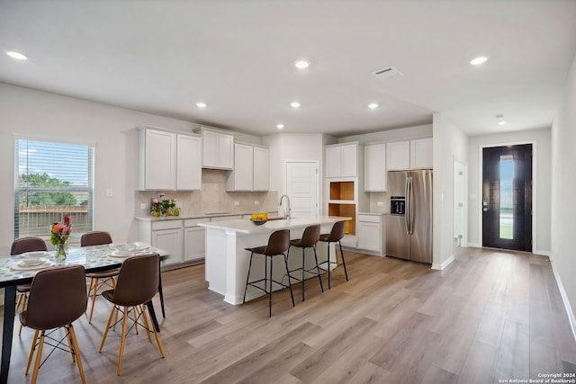 kitchen featuring white cabinets, sink, stainless steel refrigerator with ice dispenser, an island with sink, and light hardwood / wood-style floors