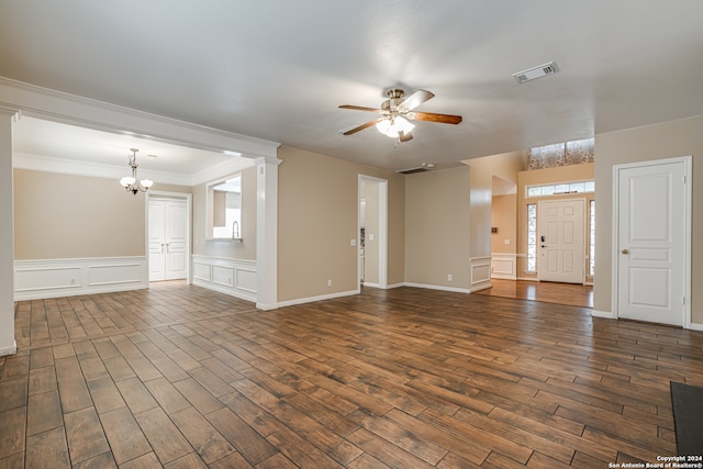 unfurnished living room featuring dark hardwood / wood-style flooring, ornate columns, crown molding, and ceiling fan with notable chandelier