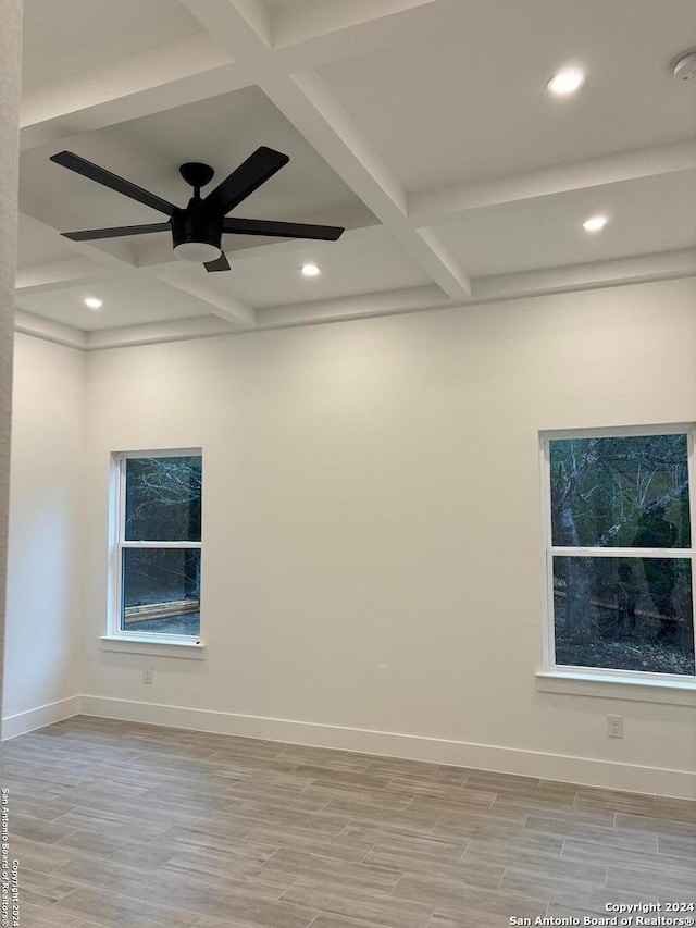 empty room featuring beamed ceiling, light wood-type flooring, ceiling fan, and plenty of natural light