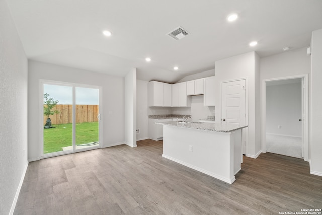 kitchen with lofted ceiling, wood-type flooring, a kitchen island with sink, light stone countertops, and white cabinetry