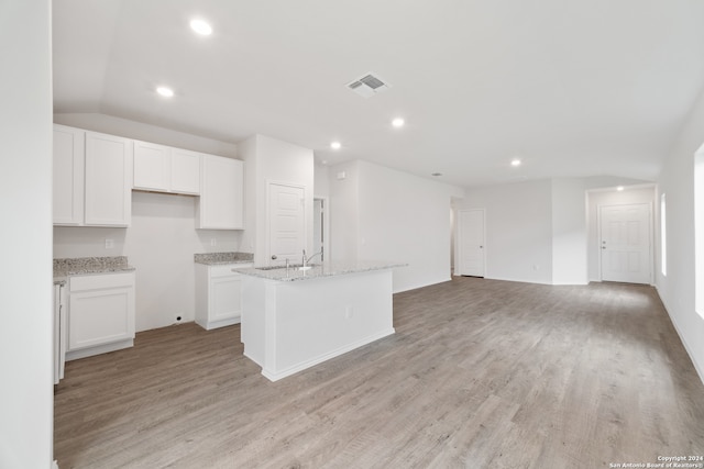 kitchen featuring light stone counters, vaulted ceiling, a kitchen island with sink, white cabinetry, and light wood-type flooring