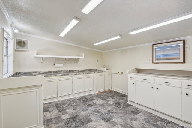 kitchen with white cabinetry, a textured ceiling, and ornamental molding