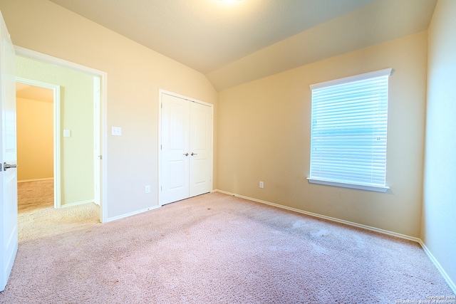 unfurnished bedroom featuring a closet, light colored carpet, and lofted ceiling