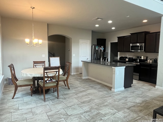 kitchen with an inviting chandelier, a center island with sink, hanging light fixtures, dark stone countertops, and stainless steel appliances