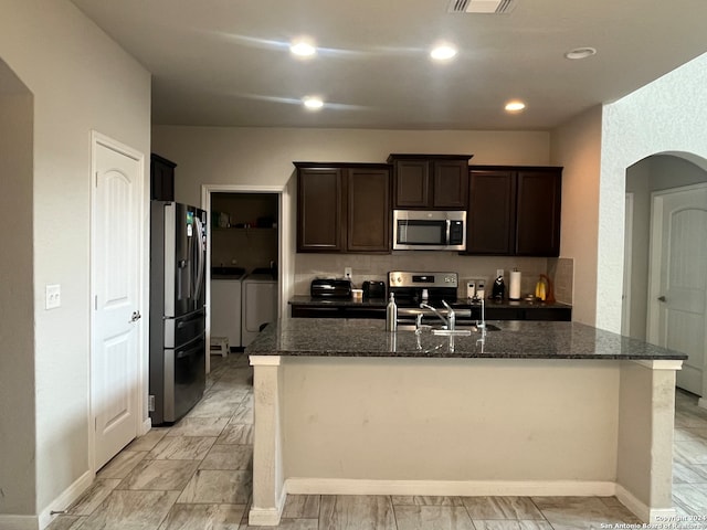 kitchen with dark stone counters, a kitchen island with sink, stainless steel appliances, and independent washer and dryer