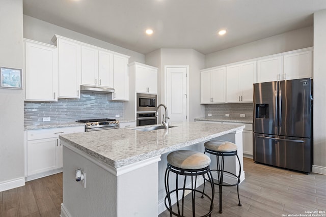 kitchen with white cabinets, appliances with stainless steel finishes, a kitchen island with sink, and light hardwood / wood-style flooring