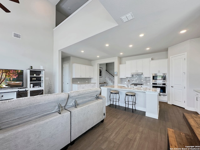 living room featuring dark wood-type flooring, sink, ceiling fan, and a towering ceiling