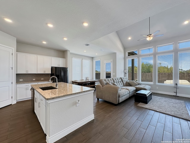 kitchen with white cabinetry, black refrigerator with ice dispenser, lofted ceiling, and an island with sink