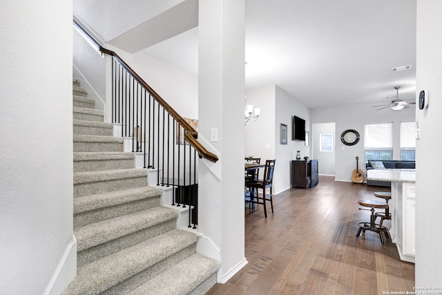 staircase featuring hardwood / wood-style floors and ceiling fan with notable chandelier