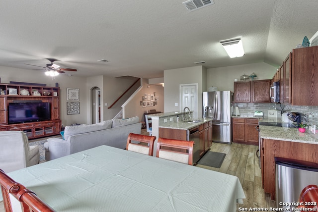 kitchen with a center island with sink, sink, appliances with stainless steel finishes, backsplash, and light wood-type flooring