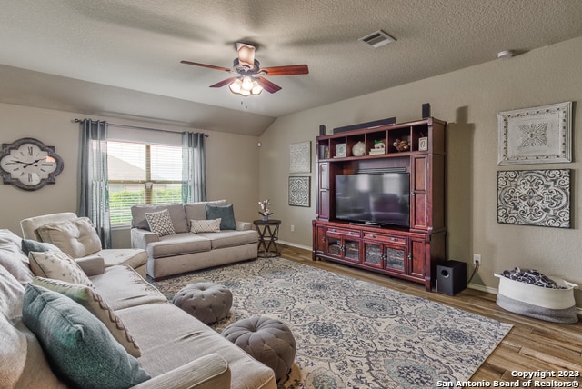 living room with a textured ceiling, hardwood / wood-style floors, lofted ceiling, and ceiling fan