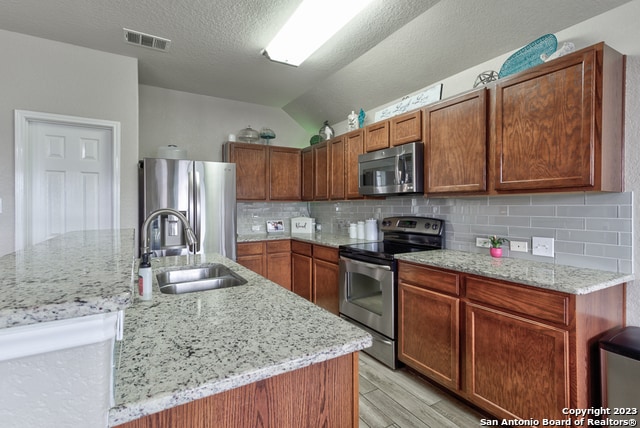 kitchen with tasteful backsplash, a center island with sink, stainless steel appliances, sink, and lofted ceiling