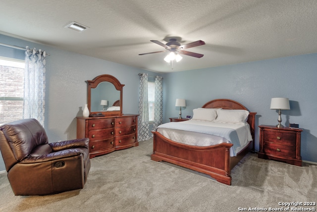 bedroom with a textured ceiling, light colored carpet, and ceiling fan