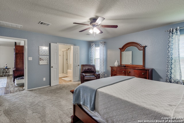 bedroom featuring a textured ceiling, light carpet, ceiling fan, and ensuite bathroom