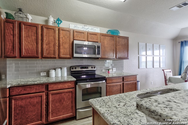 kitchen featuring light stone counters, vaulted ceiling, decorative backsplash, and appliances with stainless steel finishes