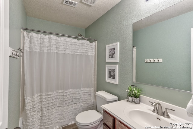 full bathroom featuring vanity, a textured ceiling, toilet, and shower / bathtub combination with curtain