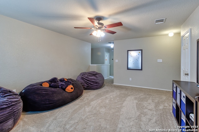 sitting room featuring ceiling fan, a textured ceiling, and light carpet