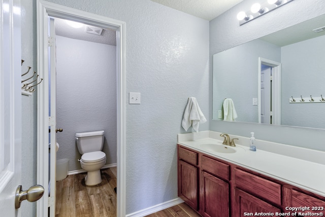 bathroom with toilet, vanity, wood-type flooring, and a textured ceiling