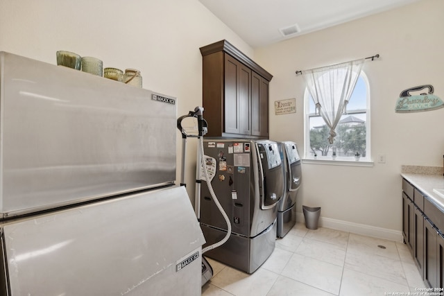 clothes washing area with separate washer and dryer, cabinets, and light tile patterned floors