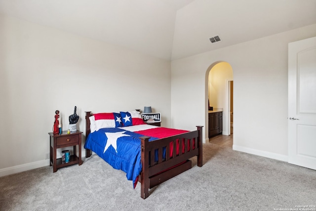 bedroom featuring light carpet, vaulted ceiling, and connected bathroom