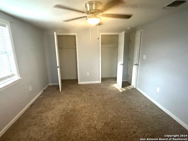 unfurnished bedroom featuring carpet, two closets, and ceiling fan