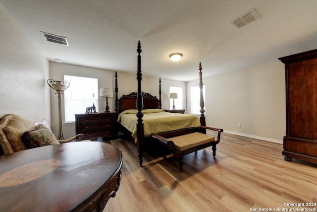 bedroom featuring a textured ceiling, light hardwood / wood-style floors, and multiple windows